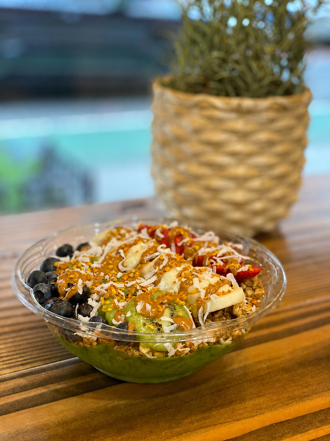 Green açai bowl topped with blueberries, kiwi, banana, strawberries, coconut, and nut butter