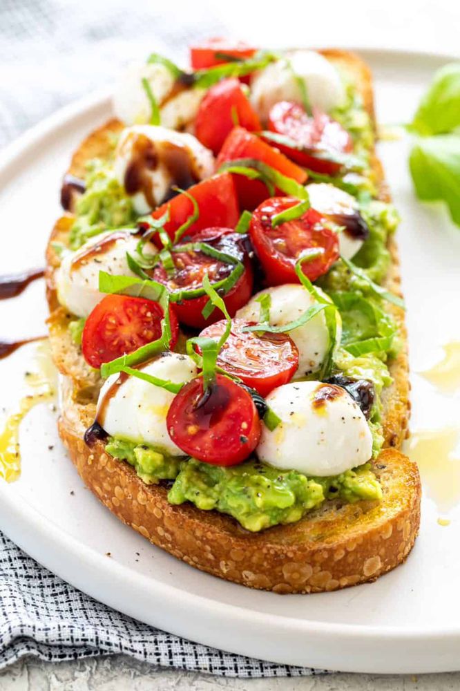 Avocado toast topped with tomatoes, mozzarella, basil, and balsamic